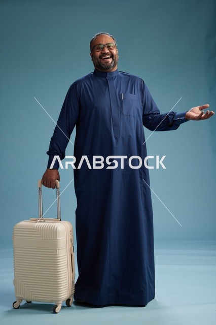 بورتيه لرجل  عربي سعودي  خليجي بثوب أزرق واقف مع حقيبة سفر, الاستعداد للسفر  والسياحه, الجسم بالطول الكامل, خلفيه زرقاء