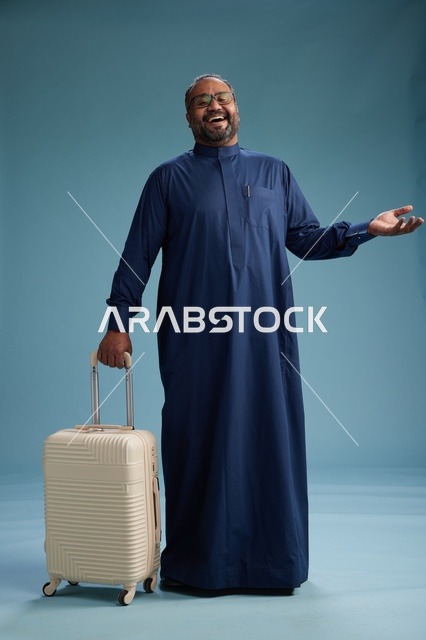 بورتيه لرجل  عربي سعودي  خليجي بثوب أزرق واقف مع حقيبة سفر, الاستعداد للسفر  والسياحه, الجسم بالطول الكامل, خلفيه زرقاء