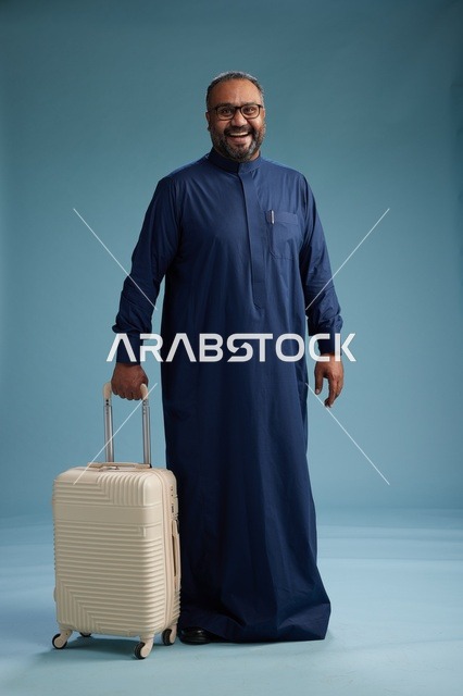 بورتيه لرجل  عربي سعودي  خليجي بثوب أزرق واقف مع حقيبة سفر, الاستعداد للسفر  والسياحه, الجسم بالطول الكامل, خلفيه زرقاء
