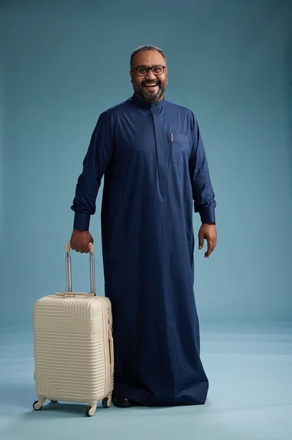 بورتيه لرجل  عربي سعودي  خليجي بثوب أزرق واقف مع حقيبة سفر, الاستعداد للسفر  والسياحه, الجسم بالطول الكامل, خلفيه زرقاء