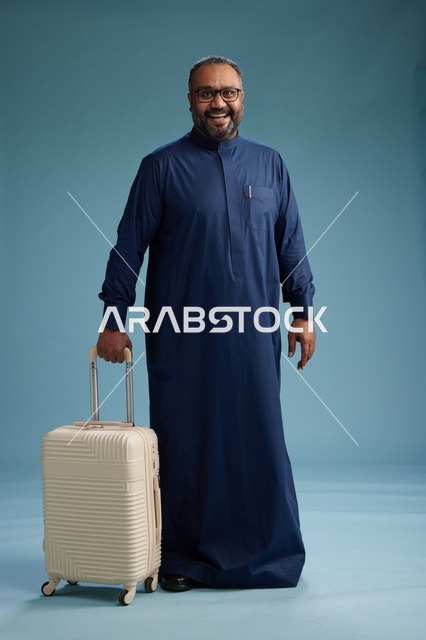 بورتيه لرجل  عربي سعودي  خليجي بثوب أزرق واقف مع حقيبة سفر, الاستعداد للسفر  والسياحه, الجسم بالطول الكامل, خلفيه زرقاء