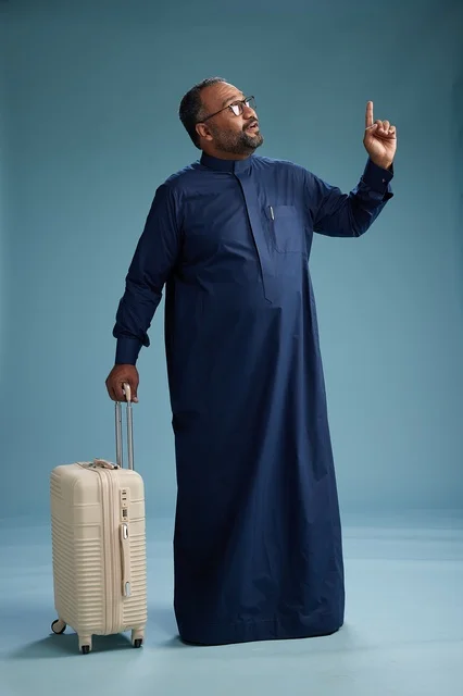 بورتيه لرجل  عربي سعودي  خليجي بثوب أزرق واقف مع حقيبة سفر, الاستعداد للسفر  والسياحه, الجسم بالطول الكامل, خلفيه زرقاء