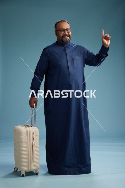 بورتيه لرجل  عربي سعودي  خليجي بثوب أزرق واقف مع حقيبة سفر, الاستعداد للسفر  والسياحه, الجسم بالطول الكامل, خلفيه زرقاء