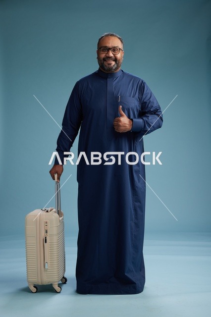 بورتيه لرجل  عربي سعودي  خليجي بثوب أزرق واقف مع حقيبة سفر, الاستعداد للسفر  والسياحه, الجسم بالطول الكامل, خلفيه زرقاء