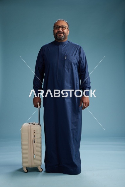 بورتيه لرجل  عربي سعودي  خليجي بثوب أزرق واقف مع حقيبة سفر, الاستعداد للسفر  والسياحه, الجسم بالطول الكامل, خلفيه زرقاء