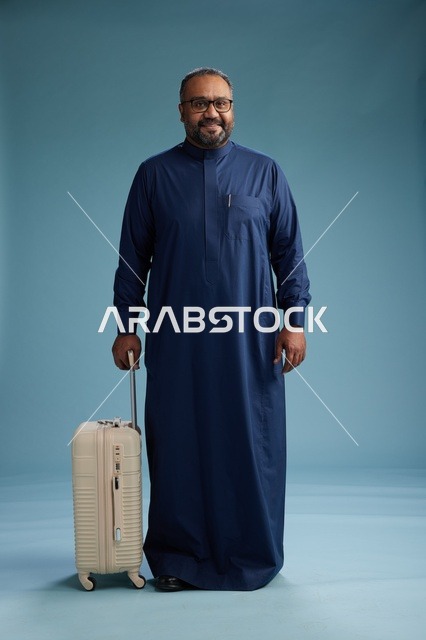 بورتيه لرجل  عربي سعودي  خليجي بثوب أزرق واقف مع حقيبة سفر, الاستعداد للسفر  والسياحه, الجسم بالطول الكامل, خلفيه زرقاء