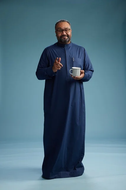 A portrait of a Saudi Arabian Gulf man in a blue thobe holding a cup of coffee and smiling, enjoying the hot drink, full-body shot, with a blue background.