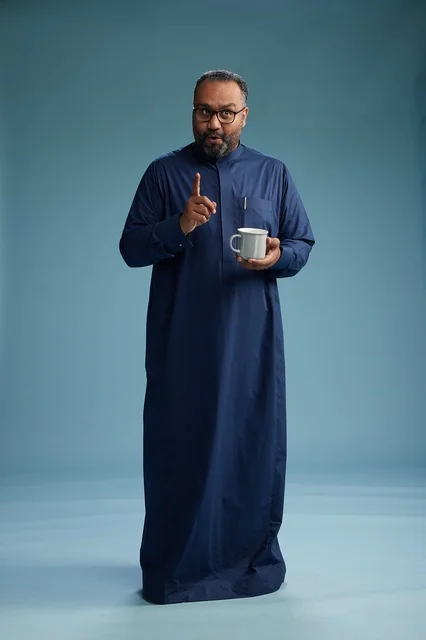 A portrait of a Saudi Arabian Gulf man in a blue thobe holding a cup of coffee and smiling, enjoying the hot drink, full-body shot, with a blue background.