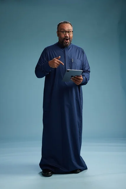 بورتريه لرجل عربي سعودي  خليجي بثوب أزرق يستخدم جهاز لوحي, استخدام التابليت المحمول, العمل اونلاين, الجسم بالكامل, خلفيه زرقاء