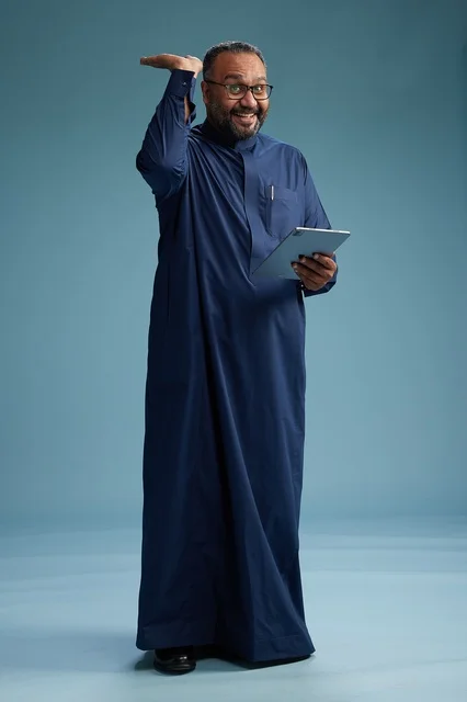 Portrait of a Saudi Arabian Gulf man in a blue thobe using a tablet, using a mobile tablet, working online, full body, blue background.
