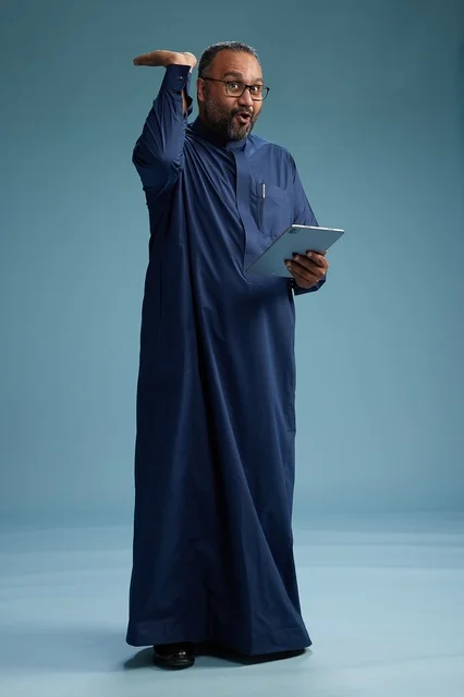 Portrait of a Saudi Arabian Gulf man in a blue thobe using a tablet, using a mobile tablet, working online, full body, blue background.