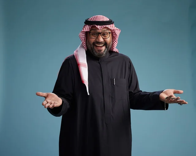 A smiling Saudi man wearing a black thobe with a shemagh and agal, with various hand gestures and movements, against a blue background.