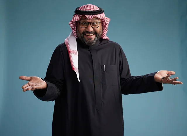 A smiling Saudi man wearing a black thobe with a shemagh and agal, with various hand gestures and movements, against a blue background.