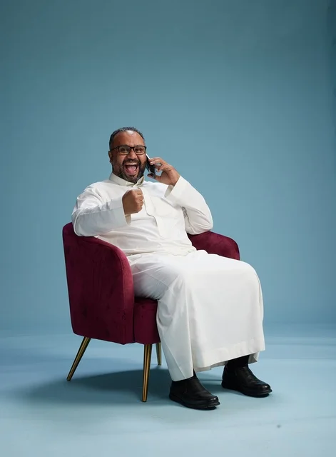 بورتريه لرجل سعودي بالزي التقليدي جالس ويتحدث في الهاتف, اجراء مكامله هاتفيه عبر الجوال , خلفيه زرقاء