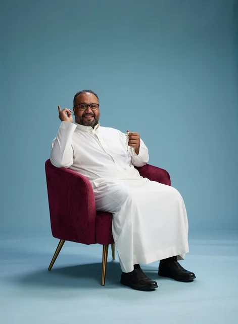 بورتريه لرجل  عربي سعودي  خليجي يرتدي الثوب الابيض يجلس على كرسي احمر,  إيماءة تعبيرية متنوعه, خلفيه زرقاء