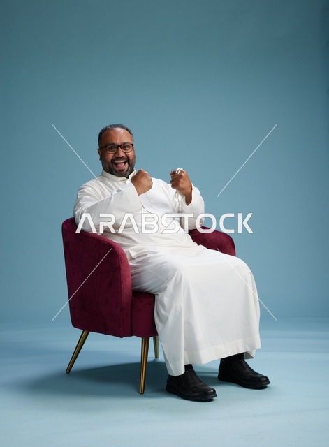 بورتريه لرجل  عربي سعودي  خليجي يرتدي الثوب الابيض يجلس على كرسي احمر,  إيماءة تعبيرية متنوعه, خلفيه زرقاء