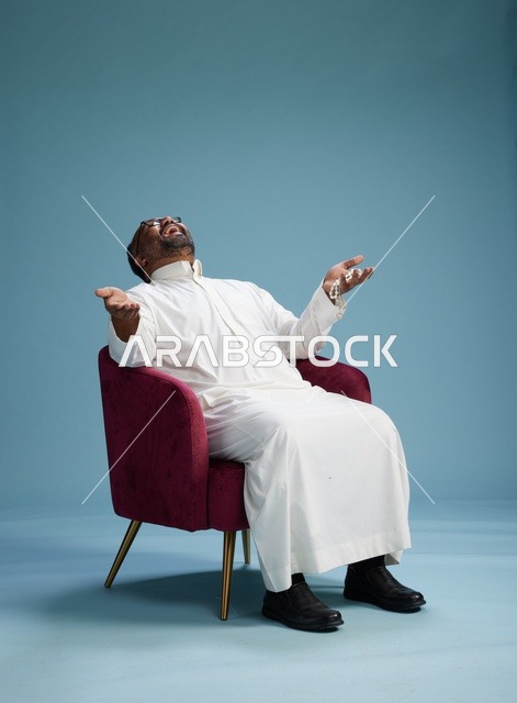بورتريه لرجل  عربي سعودي  خليجي يرتدي الثوب الابيض يجلس على كرسي احمر,  إيماءة تعبيرية متنوعه, خلفيه زرقاء