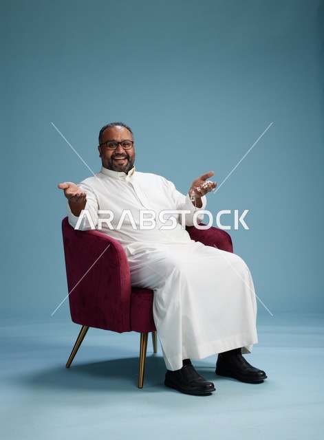 بورتريه لرجل  عربي سعودي  خليجي يرتدي الثوب الابيض يجلس على كرسي احمر,  إيماءة تعبيرية متنوعه, خلفيه زرقاء