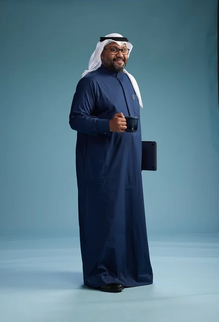 A smiling Saudi man wearing a navy blue thobe and a white ghutrah is holding a cup of coffee and a laptop, going to work, full body, blue background.