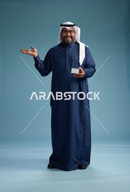 بورتريه لرجل سعودي يرتدي ثوب كحلي وغتره بيضاء يحمل بطاقة ائتمان ويقف, الجسم بالكامل, بطاقه بيضاء فارغه, خلفيه زرقاء