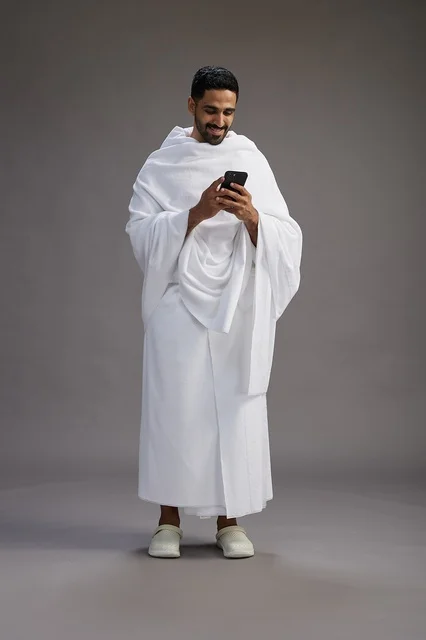 بورتريه لرجل عربي سعودي خليجي يرتدي ملابس الإحرام يستخدم الهاتف المحمول, مفهوم الحج والعمره , كامل الجسم, خلفيه رماديه بورتريه لرجل عربي سعودي خليجي يرتدي ملابس الإحرام يستخدم الهاتف المحمول, مفهوم الحج والعمره , كامل الجسم, خلفيه رماديه
