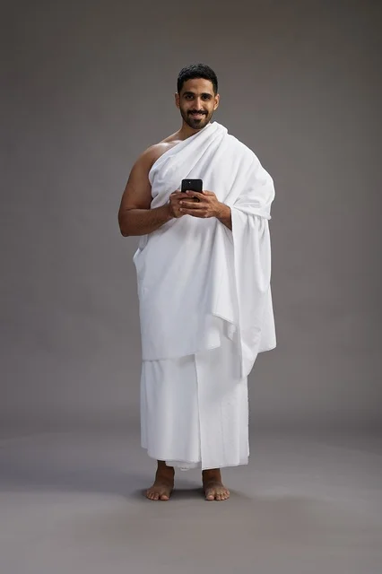 A portrait of an Arab Saudi Gulf man wearing Ihram clothing using a mobile phone, concept of Hajj and Umrah, full body, gray background. A portrait of an Arab Saudi Gulf man wearing Ihram clothing using a mobile phone, concept of Hajj and Umrah, full body, gray background.