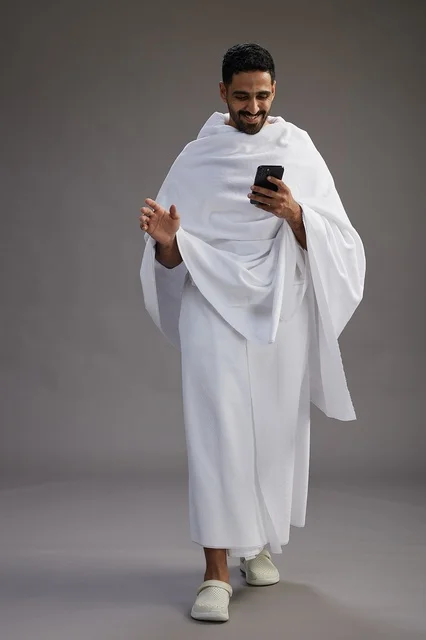 A portrait of an Arab Saudi Gulf man wearing Ihram clothing using a mobile phone, concept of Hajj and Umrah, full body, gray background. A portrait of an Arab Saudi Gulf man wearing Ihram clothing using a mobile phone, concept of Hajj and Umrah, full body, gray background.