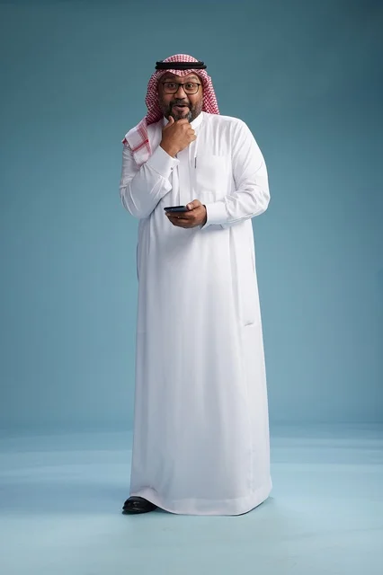 A portrait of a Saudi Arabian Gulf man wearing a white thobe and a shemagh using a smartphone, with various gestures and movements, full-body, blue background. A portrait of a Saudi Arabian Gulf man wearing a white thobe and a shemagh using a smartphone, with various gestures and movements, full-body, blue background.