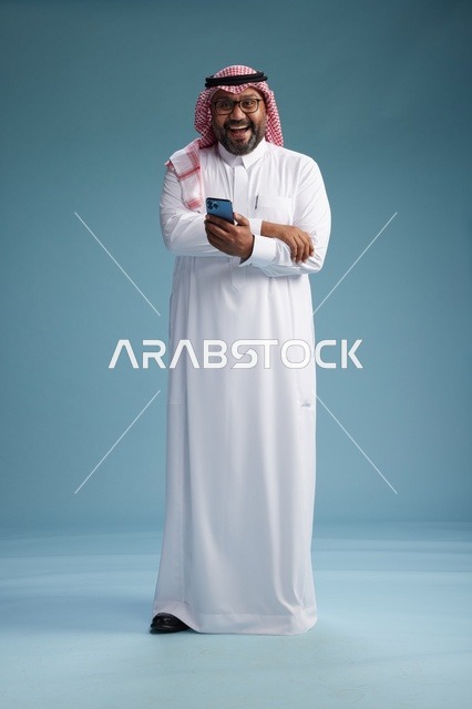 بورتريه لرجل  عربي سعودي  خليجي يرتدي الثوب الابيض والشماغ يستخدم الهاتف الذكي, ايماءات وحركات متنوعه , الجسم بالطول الكامل, خلفيه زرقاء