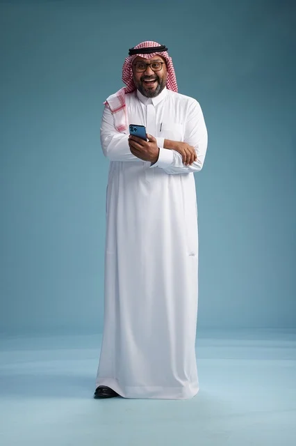 بورتريه لرجل  عربي سعودي  خليجي يرتدي الثوب الابيض والشماغ يستخدم الهاتف الذكي, ايماءات وحركات متنوعه , الجسم بالطول الكامل, خلفيه زرقاء