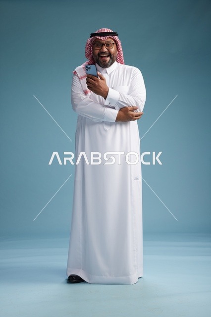بورتريه لرجل  عربي سعودي  خليجي يرتدي الثوب الابيض والشماغ يستخدم الهاتف الذكي, ايماءات وحركات متنوعه , الجسم بالطول الكامل, خلفيه زرقاء