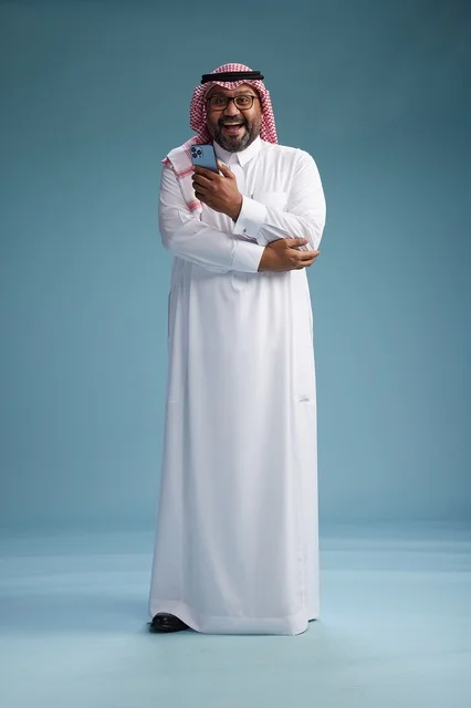 A portrait of a Saudi Arabian Gulf man wearing a white thobe and a shemagh using a smartphone, with various gestures and movements, full-body, blue background.