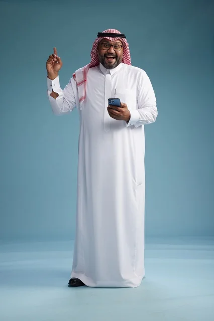 A portrait of a Saudi Arabian Gulf man wearing a white thobe and a shemagh using a smartphone, with various gestures and movements, full-body, blue background. A portrait of a Saudi Arabian Gulf man wearing a white thobe and a shemagh using a smartphone, with various gestures and movements, full-body, blue background.