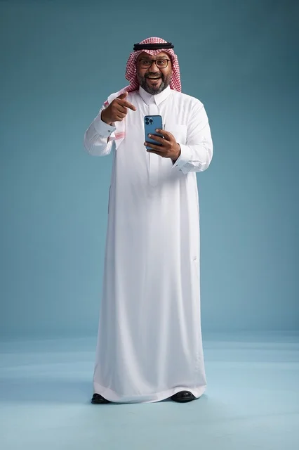 A portrait of a Saudi Arabian Gulf man wearing a white thobe and a shemagh using a smartphone, with various gestures and movements, full-body, blue background.