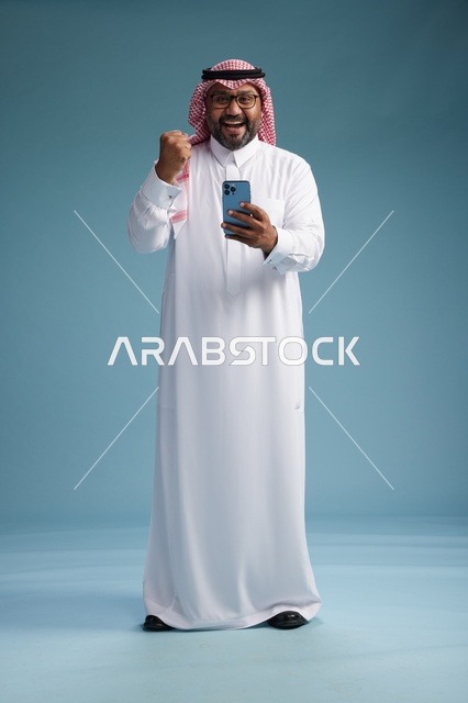A portrait of a Saudi Arabian Gulf man wearing a white thobe and a shemagh using a smartphone, with various gestures and movements, full-body, blue background.