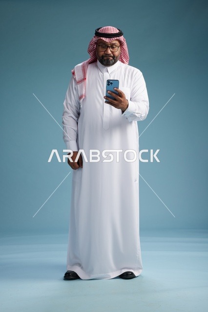 بورتريه لرجل  عربي سعودي  خليجي يرتدي الثوب الابيض والشماغ يستخدم الهاتف الذكي, ايماءات وحركات متنوعه , الجسم بالطول الكامل, خلفيه زرقاء