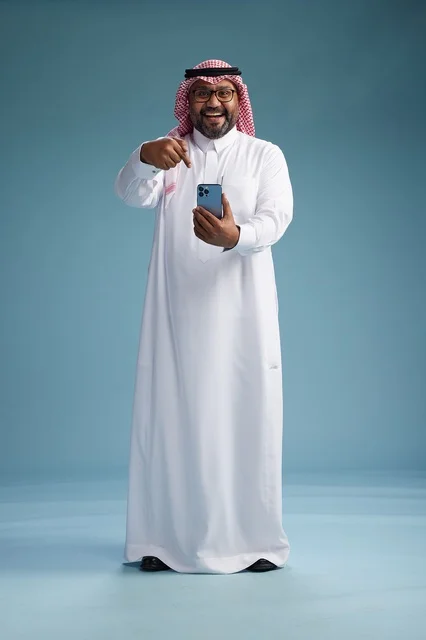 بورتريه لرجل  عربي سعودي  خليجي يرتدي الثوب الابيض والشماغ يستخدم الهاتف الذكي, ايماءات وحركات متنوعه , الجسم بالطول الكامل, خلفيه زرقاء