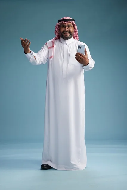 A portrait of a Saudi Arabian Gulf man wearing a white thobe and a shemagh using a smartphone, with various gestures and movements, full-body, blue background.