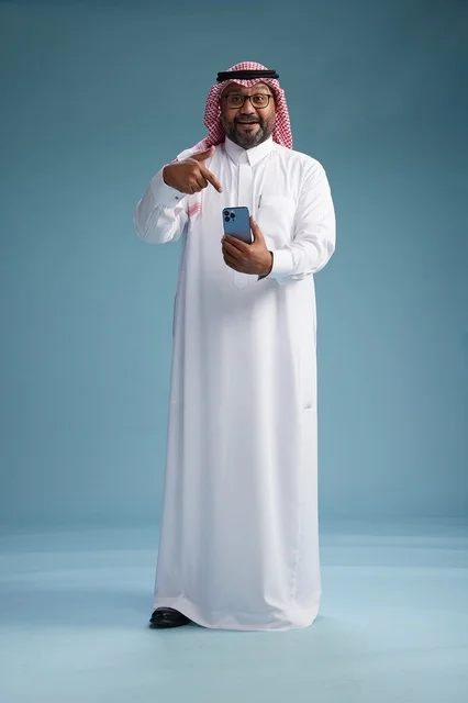 A portrait of a Saudi Arabian Gulf man wearing a white thobe and a shemagh using a smartphone, with various gestures and movements, full-body, blue background.