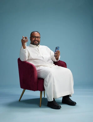 A Saudi man wearing a white thobe sits on a red chair using a mobile phone, with various movements and gestures, against a blue background.