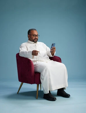 A Saudi man wearing a white thobe sits on a red chair using a mobile phone, with various movements and gestures, against a blue background. A Saudi man wearing a white thobe sits on a red chair using a mobile phone, with various movements and gestures, against a blue background.