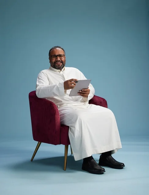 A Saudi man in traditional attire holding a tablet, using the mobile tablet, various gestures and movements, blue background.