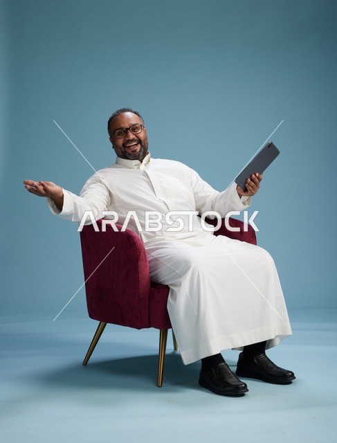 رجل سعودي بالزي التقليدي يحمل جهاز لوحي, استخدام التابليت المحمول, ايماءات وحركات متنوعه, خلفيه زرقاء