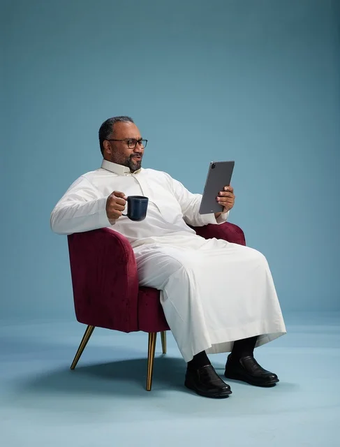 A Saudi man in traditional attire holding a tablet, using the mobile tablet, various gestures and movements, blue background.