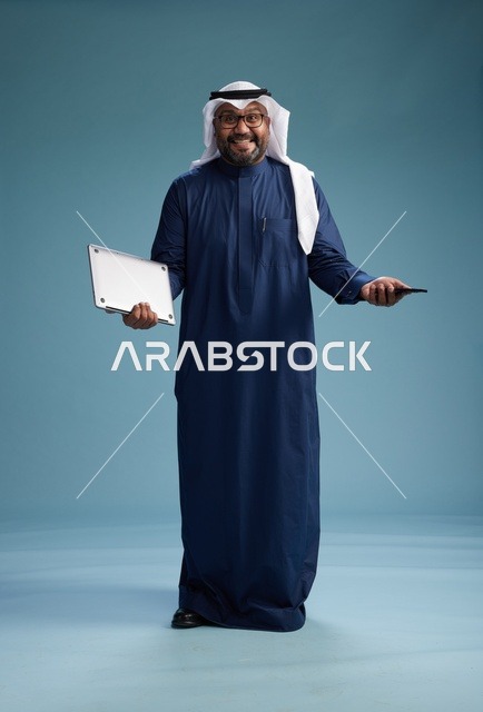 بورتريه لرجل سعودي مبتسم  يرتدي ثوب كحلي وغتره بيضاء يحمل لابتوب وهاتف ذكي, استخدام التقنيه الحديثه, كامل الجسم, خلفيه زرقاء