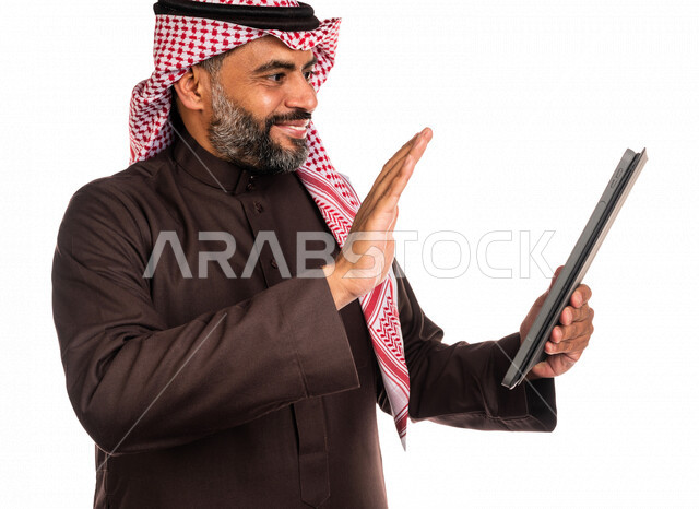 Portrait of a Saudi Arabian Gulf man holding a portable tablet, making online video calls, social communication, conversations and chatting, communicating with friends, remote business meeting, video call, live video broadcasting, white background