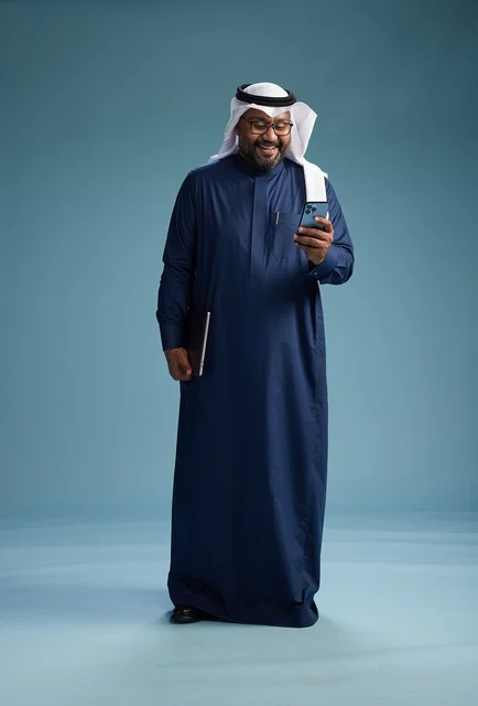 A portrait of a smiling Saudi man wearing a navy blue thobe and a white ghutrah, holding a laptop and a smartphone, using modern technology, full body, with a blue background. A portrait of a smiling Saudi man wearing a navy blue thobe and a white ghutrah, holding a laptop and a smartphone, using modern technology, full body, with a blue background.