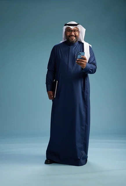 A portrait of a smiling Saudi man wearing a navy blue thobe and a white ghutrah, holding a laptop and a smartphone, using modern technology, full body, with a blue background. A portrait of a smiling Saudi man wearing a navy blue thobe and a white ghutrah, holding a laptop and a smartphone, using modern technology, full body, with a blue background.
