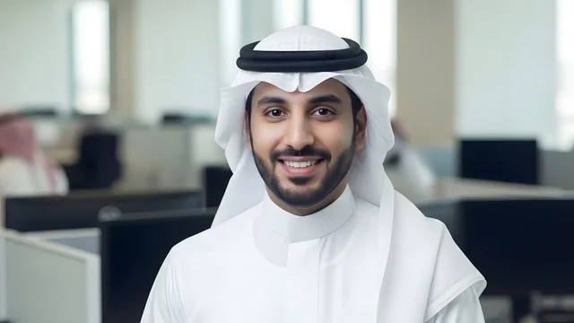 Looking at the camera with expressions of joy, business technology in the United Arab Emirates, a close-up shot of a smiling Emirati employee wearing the kandura and white ghutrah in a modern office, a professional work environment, the concept of perfection and focus.