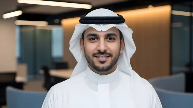 النظر الى الكاميرا بتعابير السرور ، تكنولوجيا الأعمال في الامارات العربيه المتحده، تصوير مقرب لموظف امارتي مبتسم يرتدي الكندورة والغترة البيضاء في مكتب عصري، بيئة عمل احترافية، مفهوم الإتقان والتركيز